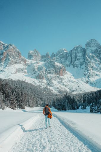 A beautiful view of a person walking in the field covered in snow with the mountain in the background