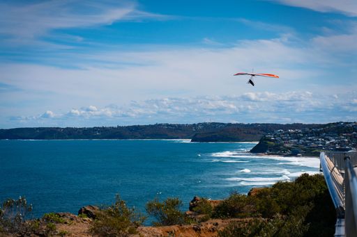 A hang glider soaring over a tranquil azure sea on a clear, sunny summer day