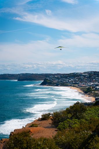 A hang glider soaring over a tranquil azure sea on a clear, sunny summer day