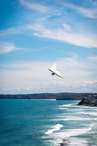 A hang glider soaring over a tranquil azure sea on a clear, sunny summer day