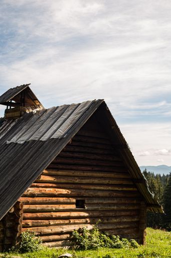 A vertical of a wooden house on the grassy field under the cloudy blue sky in the rural area