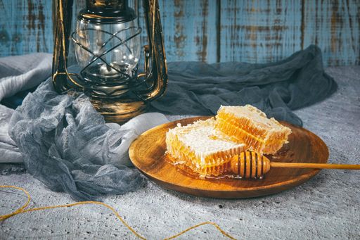 A closeup of a wooden dipper on a wooden plate of honeycomb pieces on background of a vintage lantern