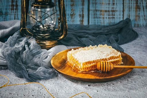A closeup of a wooden dipper on a wooden plate of honeycomb pieces on background of a vintage lantern