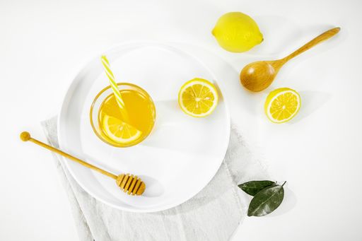 A top view of a lemon juice glass next to wooden honey dipper on a white plate