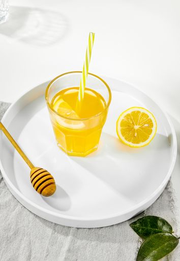 A vertical shot of a lemon juice glass next to wooden honey dipper on a white plate