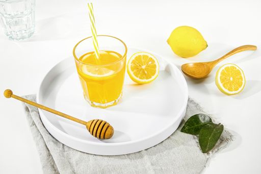 A closeup of a lemon juice glass next to wooden honey dipper on a white plate