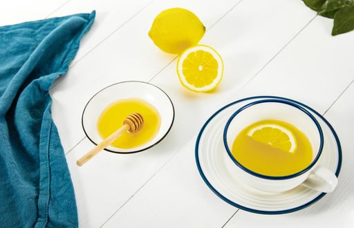 A closeup of a lemon tea next to golden honey in a bowl isolated on wooden white surface