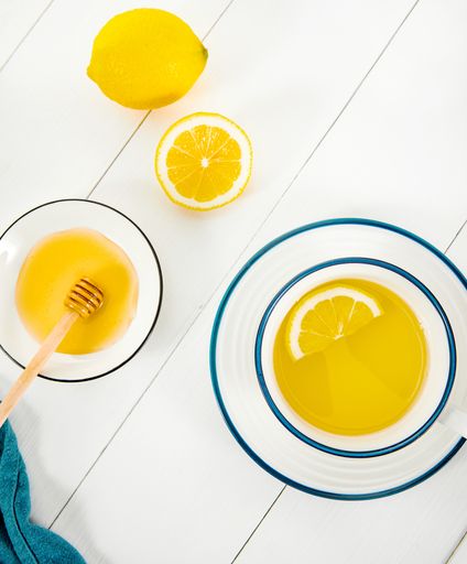 A top view of a lemon tea next to golden honey in a bowl isolated on wooden white surface
