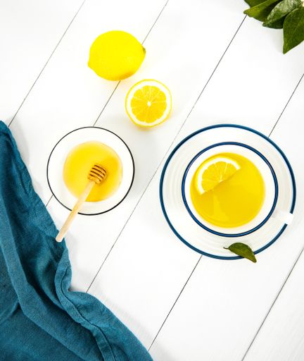 A top view of a lemon tea next to golden honey in a bowl isolated on wooden white surface