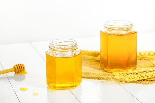 A closeup of golden honey jars next to a dipper isolated on white background