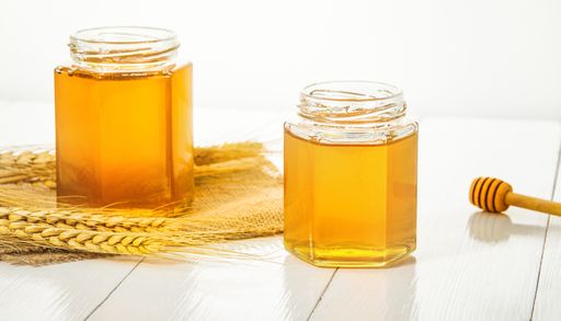 A closeup of golden honey jars next to a dipper isolated on white background