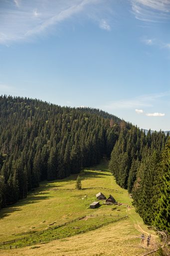 A beautiful landscape with buildings on the grassy hill surrounded by trees under the blue sky