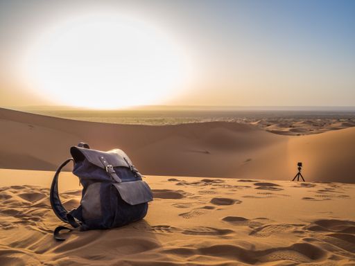 A camera and a backpack on the sandy ground in the desert at sunset