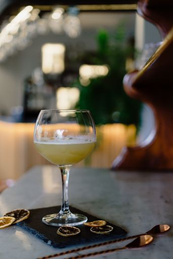 A vertical shot of an iced cocktail with dried lemons on a black board and two spoons