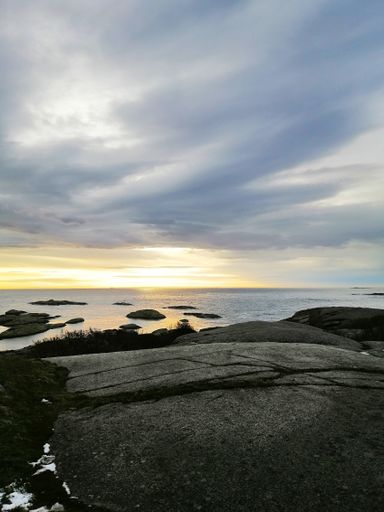 A vertical picture of rocks surrounded by the sea under a cloudy sky during the sunset in Norway