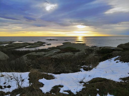 A sea surrounded by rocks under a cloudy sky during the sunset in Rakke in Norway