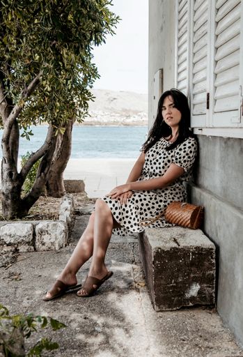 A vertical shot of a caucasian female sitting on the stone surface with an ocean in the background