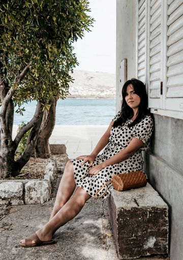 A vertical shot of a caucasian female sitting on the stone surface with an ocean in the background