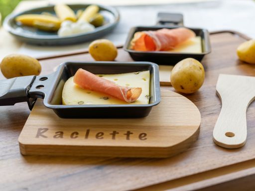A selective focus shot of raclette pepper cheese with parma ham in a grill pan on a wooden board