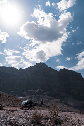 A vertical shot of a helicopter parked in the Colorado Canyon under a cloudy blue sky. Mountains, desert plants and cactus