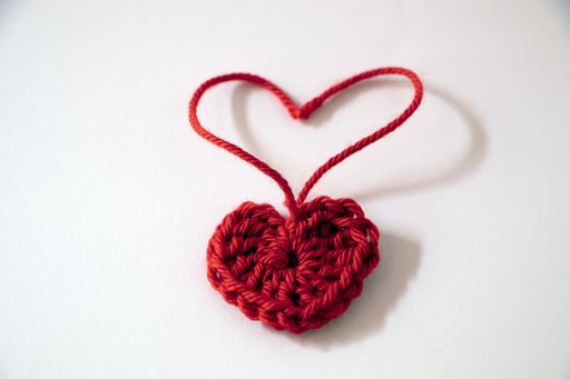 A closeup shot of a crocheted red heart on a white surface