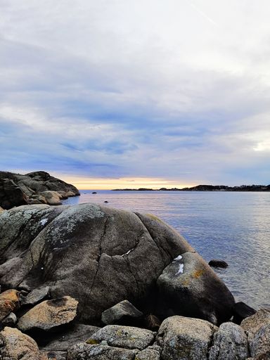 A vertical picture of the sea surrounded by rocks under a cloudy sky during the sunset in Norway