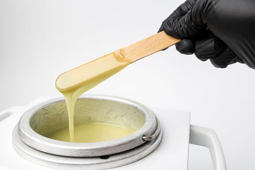 A human hand holding wooden sticks with wax over wax melter