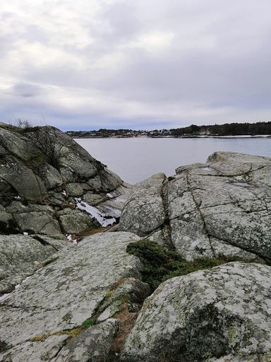 A vertical picture of rocks surrounded by the river under a cloudy sky in Norway