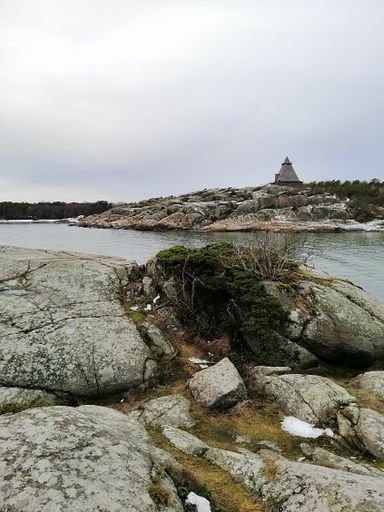 A vertical picture of rocks surrounded by the river under a cloudy sky in Norway