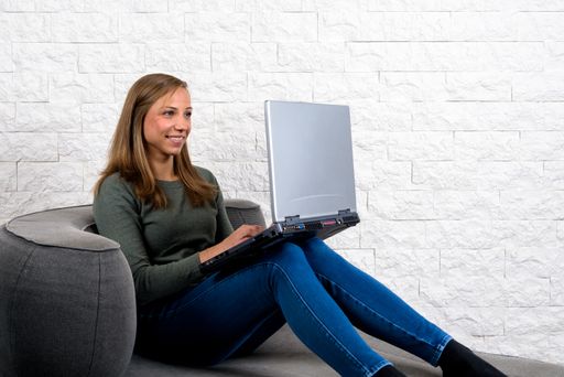 Young caucasian woman sitting working typing in home office with her laptop on legs grinning while video chat
