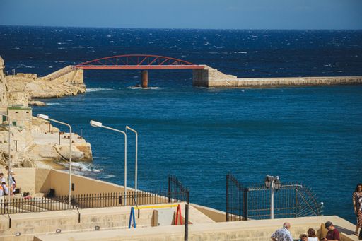 A wide angle shot of a bridge made of stone and red metal going over the water