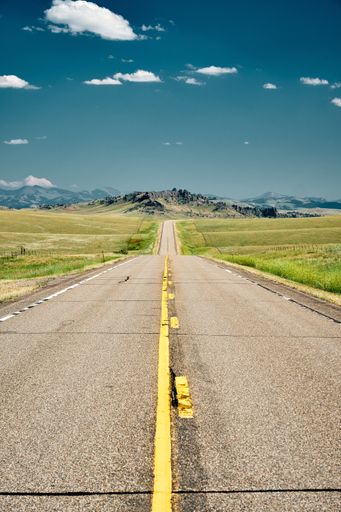 A vertical shot of a road on a green landscape under a blue sky