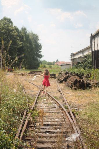 A vertical back view of a young female in a red dress running on the train tracks