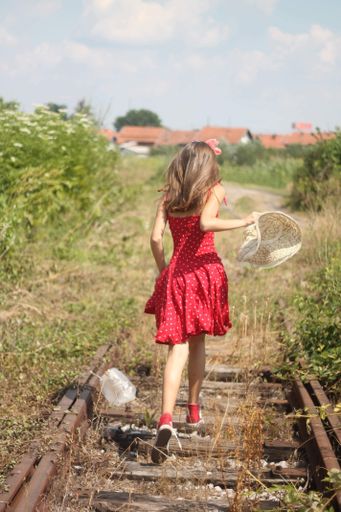 A vertical back view of a young female in a red dress running on the train tracks
