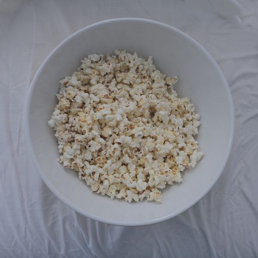 A closeup shot of popcorn in a white bowl on a bed