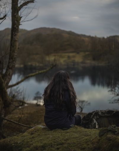A vertical shot of a lonely female sitting by the lake and enjoying the beautiful view