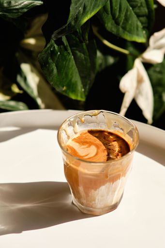 A vertical shot of the glass with coffee on the white table on a sunny day