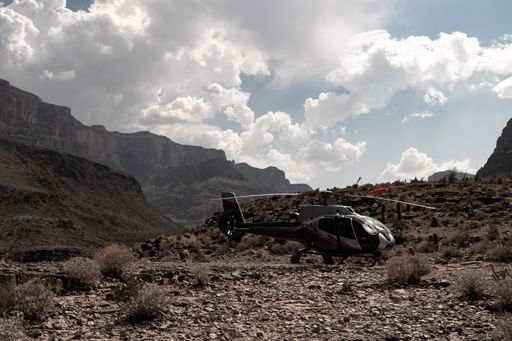 A horizontal shot of a helicopter parked in the Colorado Canyon under a cloudy blue sky. Mountains, desert plants and cactus