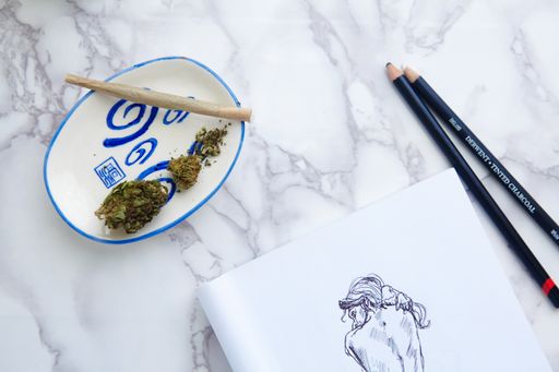 THC CBD Marijuana joint and flowers on ash tray with nude illustration on drawing pad on marble table and succulents.