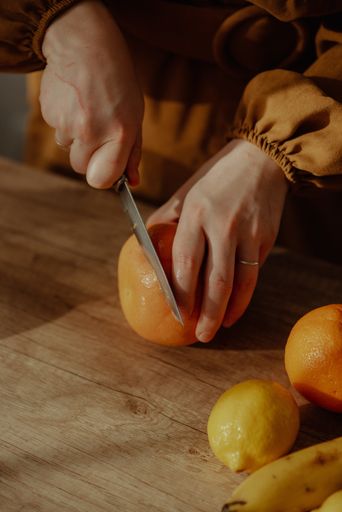 A vertical shot of a person cutting an orange on a cutting board