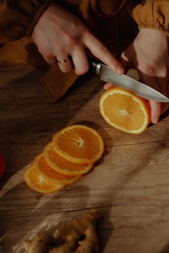A vertical shot of a person cutting an orange on a cutting board