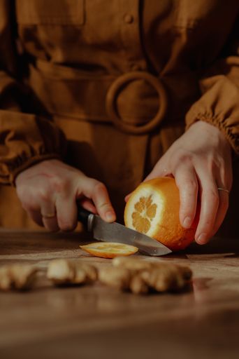 A vertical shot of a person cutting an orange on a cutting board