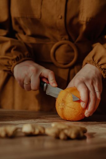 A vertical shot of a person cutting an orange on a cutting board