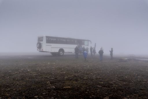 A big white bus and a group of people near it in foggy weather in Iceland