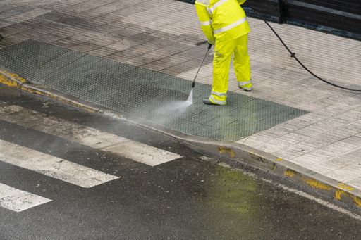 Sweeper cleaning a street sidewalk with high pressure water jet.