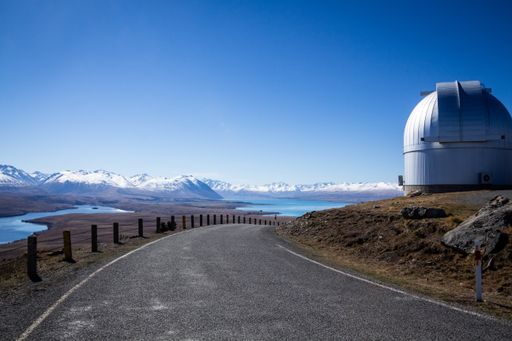a beautiful overview over lake Tekapo, New Zealand with a blue sky and a street and a observatory in the foreground.
