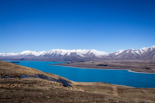 Epic shot of Lake Tekapo from a perfect point of view with snow covered mountains in the background. The water is extremely blue.