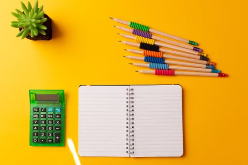 A top view of a journal, calculator, pencils, and a plant, on a yellow background