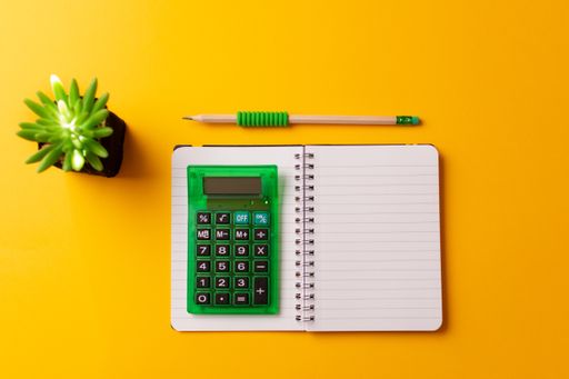 A top view of a calculator on an open journal, a pencil, and a plant on a yellow background