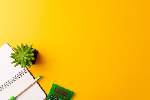 A top view of pencil on a journal, calculator, and a plant on a yellow background